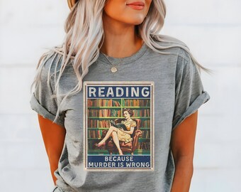 May include: A gray t-shirt with a vintage-style graphic featuring a woman reading a book in a library. The graphic says "Reading because murder is wrong."