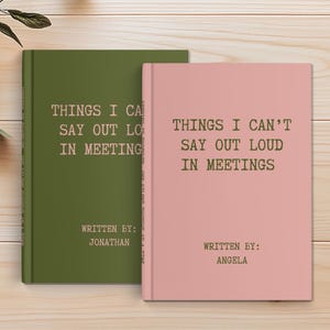 May include: Two hardcover books with the text "THINGS I CAN'T SAY OUT LOUD IN MEETINGS" on the cover. One book is olive green, the other is pink. The author's names are printed below the title. The books are on a light wood surface.