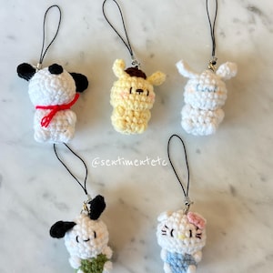 May include: Crocheted character charms featuring Snoopy, Pompompurin, Cinnamoroll, Pochacco, and Hello Kitty. Each charm is white, yellow, or blue, with black accents and a black lanyard. The text "Snoopy", "Pompompurin", "Cinnamoroll", "Pochacco", and "Hello Kitty" is displayed.