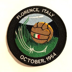 May include: A black and white embroidered patch with a soccer ball, green grass, and the text "FLORENCE, ITALY OCTOBER, 1954."