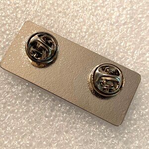 May include: The back of a silver metal pin with two metal clasps.