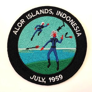 May include: A black and white embroidered patch with the text "ALOR ISLANDS, INDONESIA" and "JULY, 1959". The patch features a blue and green background with two figures in blue diving suits.