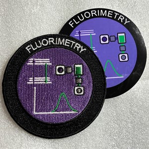 Peut inclure: Un écusson brodé circulaire et un autocollant circulaire assorti, tous deux dotés d'un fond violet, d'une bordure noire et du texte FLUORIMETRY. Le motif inclut un diagramme de niveaux d'énergie blanc, une flèche verte et un graphique à deux courbes.