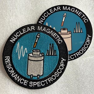 May include: Two circular patches featuring a teal background with a gray scientific instrument, a pipette, and white wave patterns. The black border contains the white text NUCLEAR MAGNETIC RESONANCE SPECTROSCOPY. The design is embroidered on fabric.