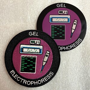 Peut inclure: Deux écussons circulaires avec un fond violet et une bordure noire. Le motif comprend une cuve d'électrophorèse blanche, un gel avec des bandes vertes et une pipette. Le texte GEL ELECTROPHORESIS est imprimé en blanc sur la bordure.