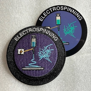 Può includere: Una toppa ricamata circolare e un adesivo circolare abbinato, entrambi con sfondo viola, bordo nero e il testo ELECTROSPINNING. Il design raffigura una siringa, una fonte di alimentazione e una rete di fibre in azzurro e bianco.