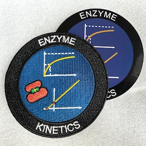 May include: A circular embroidered patch featuring a blue background, a black border, and the white text ENZYME KINETICS. The design includes two white line graphs and a red enzyme illustration. A matching circular sticker is partially visible behind it.