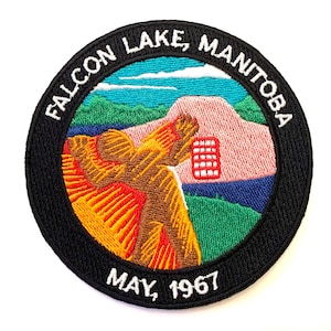 May include: Embroidered patch with a black background and white text that reads "Falcon Lake, Manitoba May, 1967". The center of the patch features a colorful embroidered landscape with a pink mountain, green trees, and a blue lake.