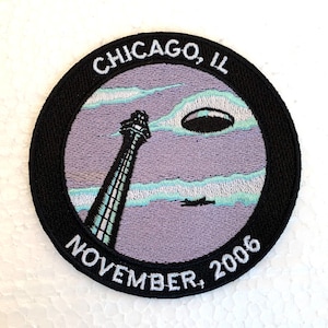 May include: Embroidered patch with a black border, a purple background, and white text. The text reads "CHICAGO, IL NOVEMBER, 2006". The patch features a white tower with a blue and white striped design, a white cloud, and a blue UFO.