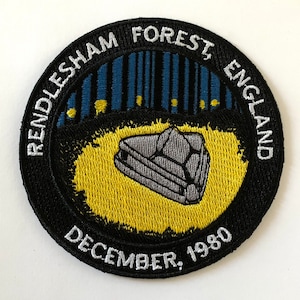 May include: A black and white embroidered patch with the text "Rendlesham Forest, England December, 1980" and a stylized image of a flying saucer in the center.