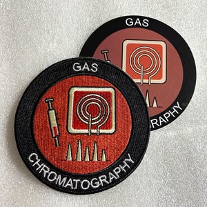 Può includere: Una toppa circolare ricamata con un centro rosso, un'icona di siringa bianca, un quadrato bianco contenente una spirale rossa e picchi bianchi sul fondo. Il bordo nero mostra il testo bianco GAS CHROMATOGRAPHY. Un adesivo abbinato si trova dietro.