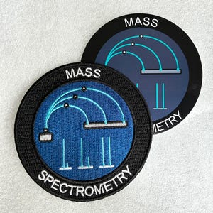 May include: Two circular patches featuring a mass spectrometry diagram. The foreground patch is embroidered with a blue center, black border, and white text reading MASS SPECTROMETRY. The background patch is a smooth sticker with similar graphics.