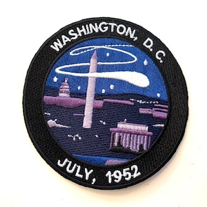 May include: A black and white embroidered patch with a blue background. The patch depicts the Washington Monument, the Capitol Building, and a comet in the sky. The text "WASHINGTON, D.C. JULY, 1952" is embroidered around the edge of the patch.