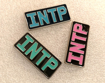May include: Three enamel pins with the letters "INTP" in different colours. The pins are black with a silver border. The letters are blue, teal, and pink.