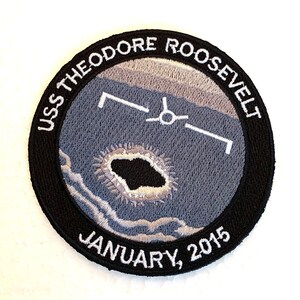 Puede incluir: Un parche bordado en blanco y negro con el texto "USS THEODORE ROOSEVELT JANUARY, 2015". El parche presenta una imagen estilizada de un portaaviones con un avión despegando.
