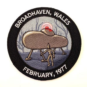 May include: A black and white embroidered patch with a UFO, a figure, and the text "BROADHAVEN, WALES FEBRUARY, 1977".
