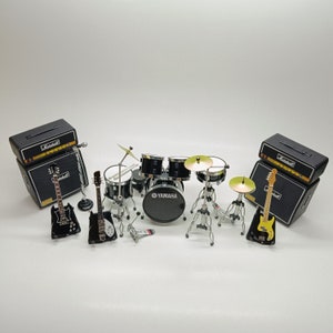 Pode incluir: Um conjunto de bateria preto em miniatura com duas guitarras elétricas, dois amplificadores pretos e uma pele de bateria Yamaha. O conjunto de bateria inclui um bumbo, uma caixa, dois tons e um prato.