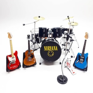 May include: A miniature drum set with a black bass drum that says "NIRVANA" with a yellow smiley face. There are three miniature guitars, one red, one brown, and one blue.