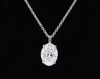 May include: A silver necklace with a delicate chain and a large, oval-shaped diamond pendant. The diamond is clear and sparkling, set in a simple, elegant setting. The necklace is displayed against a black background.