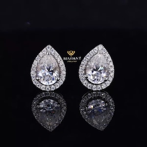May include: A pair of pear-shaped diamond earrings with a halo setting. The earrings are set in white gold and feature a sparkling diamond center stone.