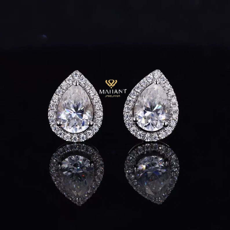 May include: A pair of pear-shaped diamond earrings with a halo setting. The earrings are set in white gold and feature a sparkling diamond center stone.