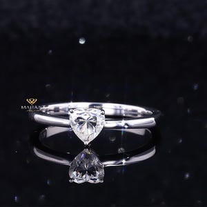 Pode incluir: Um anel solitário de prata com um diamante em forma de coração.