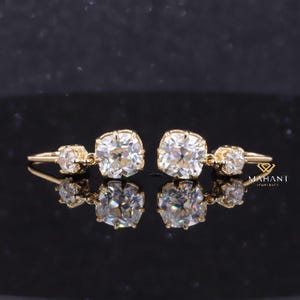 May include: A pair of gold earrings with large, square-shaped, clear gemstones. Each earring has a smaller, round, clear gemstone hanging from the larger gemstone.