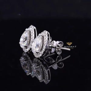 May include: A pair of pear-shaped diamond earrings with a halo setting. The earrings are set in white gold and have a polished finish.