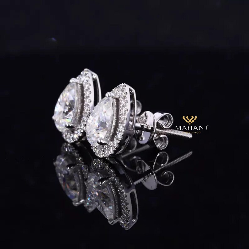 May include: A pair of pear-shaped diamond earrings with a halo setting. The earrings are set in white gold and have a polished finish.