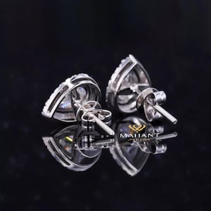 May include: A pair of pear-shaped diamond earrings with a silver setting. The earrings are set with a single pear-shaped diamond in the center, surrounded by smaller diamonds.