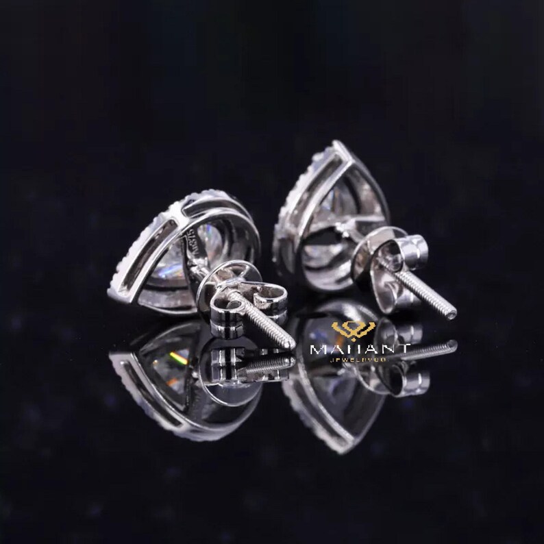 May include: A pair of pear-shaped diamond earrings with a silver setting. The earrings are set with a single pear-shaped diamond in the center, surrounded by smaller diamonds.