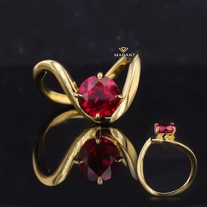 Könnte beinhalten: Ein goldener Ring mit einem großen, runden, roten Rubin-Edelstein. Der Ring hat ein einzigartiges, geschwungenes Design.
