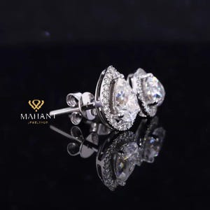 May include: A pair of pear-shaped diamond earrings with a halo setting. The earrings are set in white gold and have a polished finish.