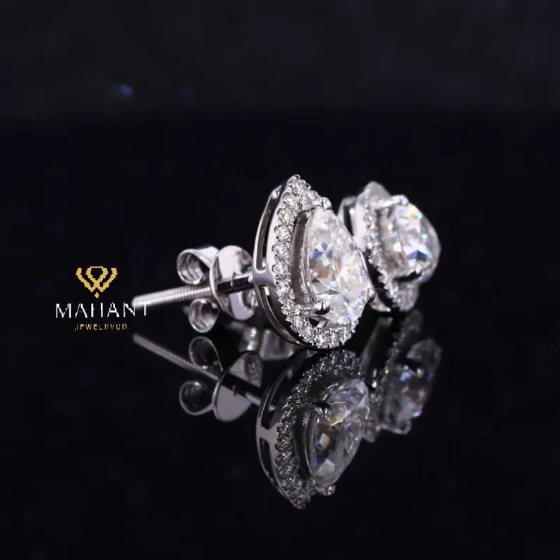 May include: A pair of pear-shaped diamond earrings with a halo setting. The earrings are set in white gold and have a polished finish.