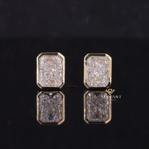 May include: A pair of gold earrings with large, clear emerald-cut cubic zirconia stones.