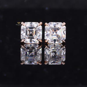 May include: A pair of square-cut, clear gemstone stud earrings with rose gold settings. The earrings are displayed on a reflective black surface, showcasing their brilliance. The MAIHAN logo is visible in the upper left corner.