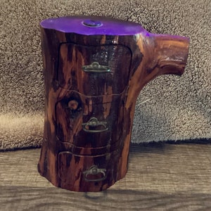 May include: A wooden jewelry box shaped like a tree trunk with three drawers. The drawers have metal handles and the top of the box is stained a dark purple color.