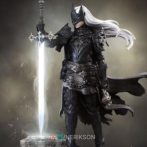 May include: A detailed figurine of a warrior in black armour, holding a glowing sword. The figure has long white hair and a mask. The armour features intricate designs, and the sword emits a bright light. The overall theme is fantasy.
