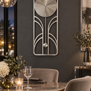 May include: A tall, rectangular wall clock made of brushed silver metal. The clock features a circular face with simple hour markers and thin hands, set within a frame that includes symmetrical, curved decorative lines and a small pendulum.