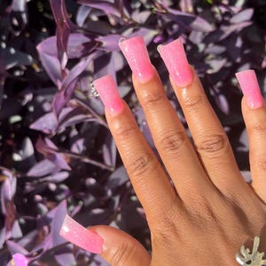 May include: Pink glitter square-shaped press-on nails with a clear base.