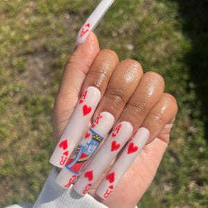 May include: White long acrylic nails with red hearts and playing card designs, including the King of Hearts.