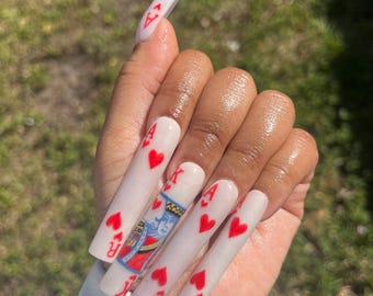 May include: White long acrylic nails with red hearts and playing card designs, including the King of Hearts.
