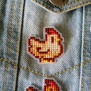 May include: A brown and orange embroidered chicken patch on a blue denim jacket.