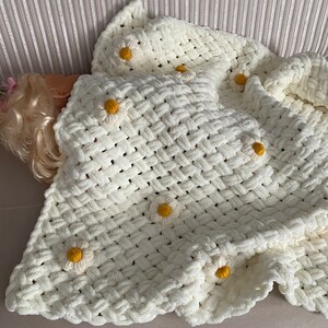 May include: A white crocheted blanket with a woven pattern and yellow daisy embellishments.