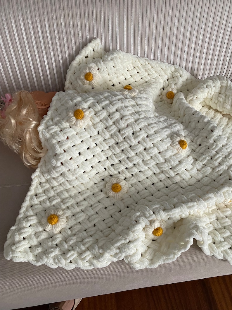 May include: A white crocheted blanket with a woven pattern and yellow daisy embellishments.