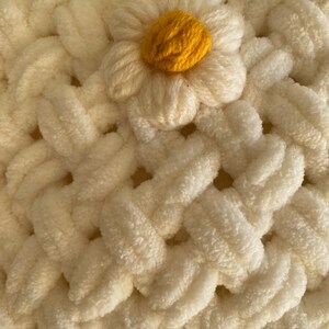 May include: A white crocheted blanket with a yellow daisy flower in the center.