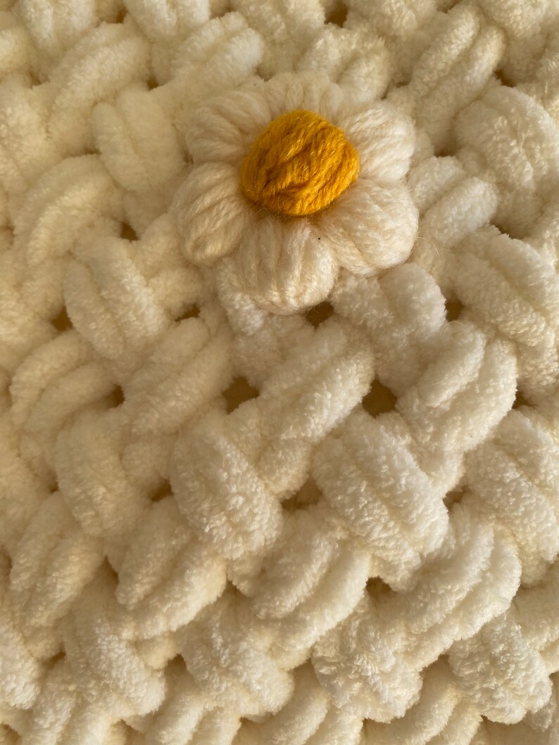 May include: A white crocheted blanket with a yellow daisy flower in the center.