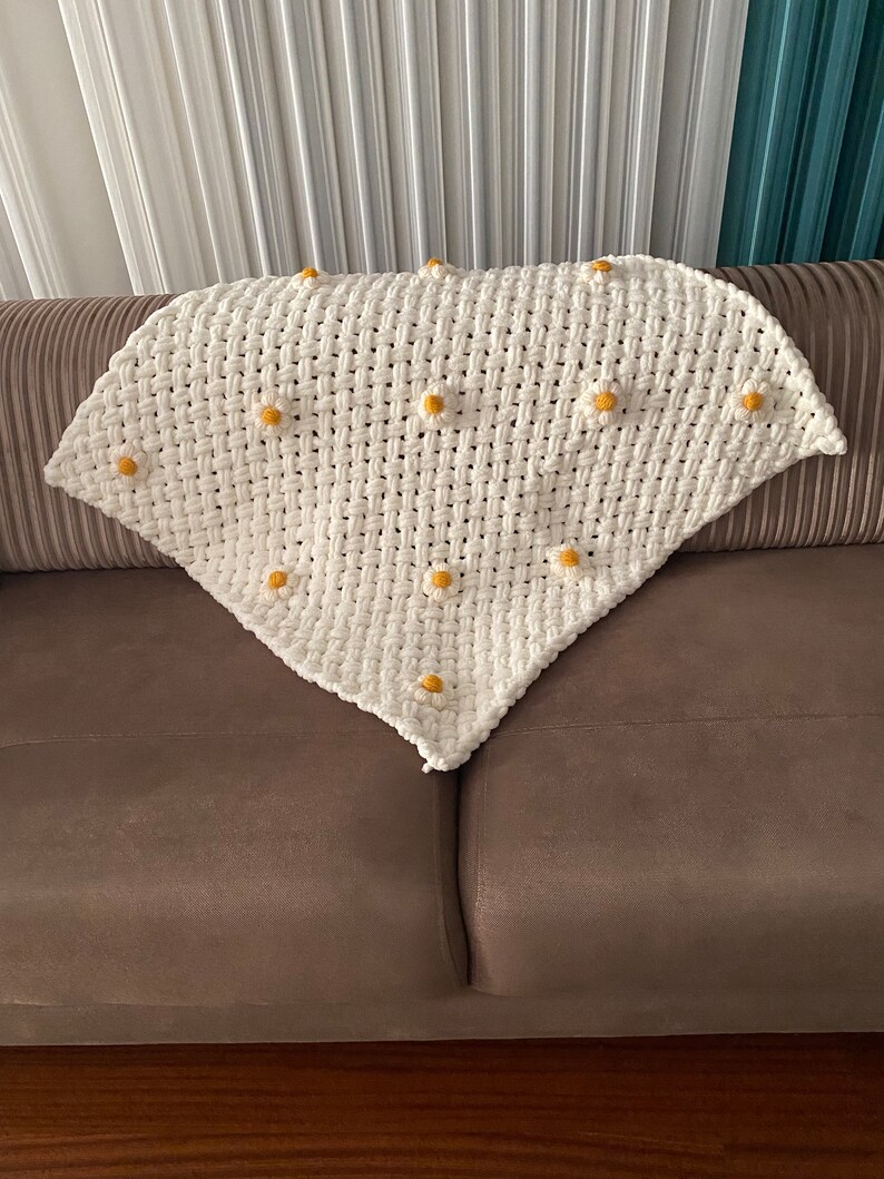 May include: A white crocheted blanket with a triangular shape and yellow daisy accents.