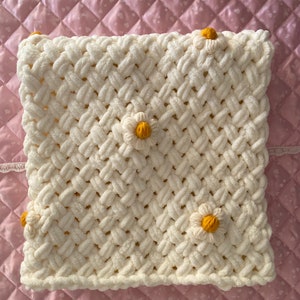 May include: White crocheted blanket with a woven pattern and yellow daisy embellishments.