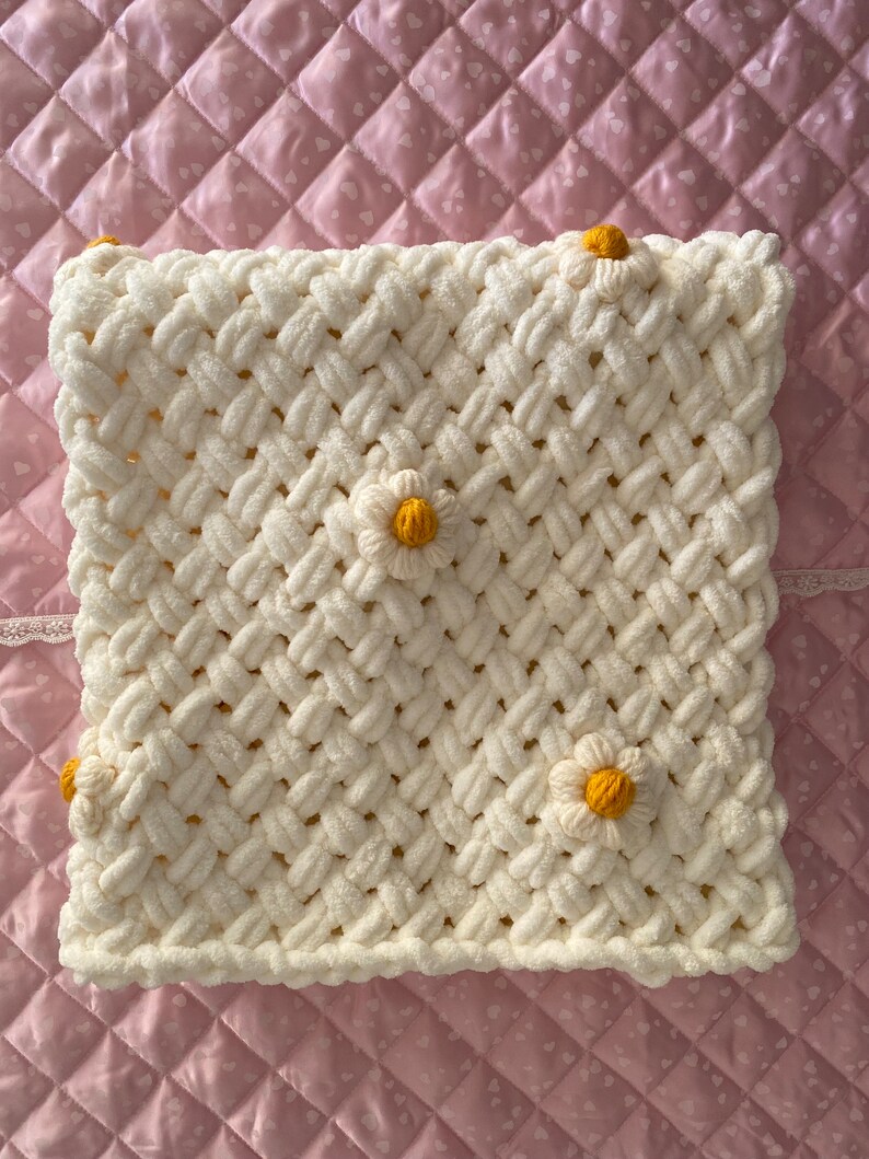 May include: White crocheted blanket with a woven pattern and yellow daisy embellishments.